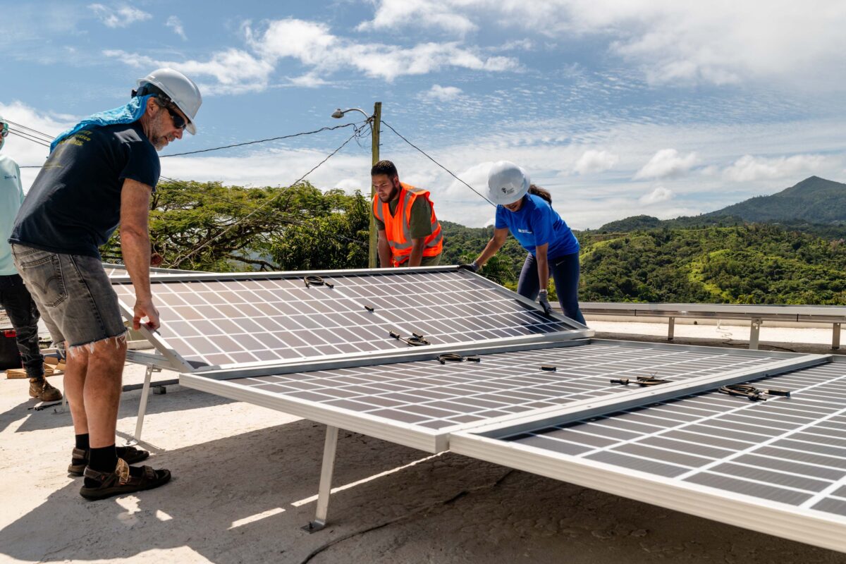 A team of four workers aligns solar panels in a rooftop array