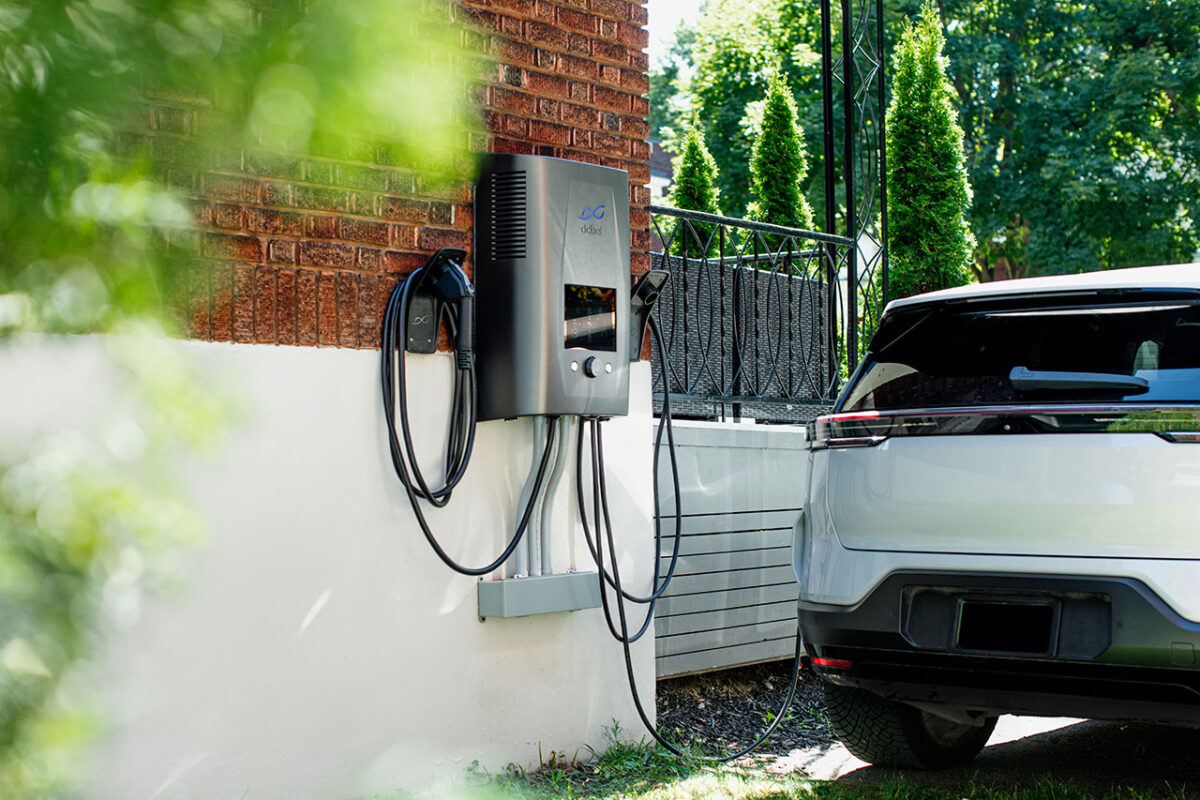 A dcbel Ara charger mounted on the side fo a home, plugged into a vehicle